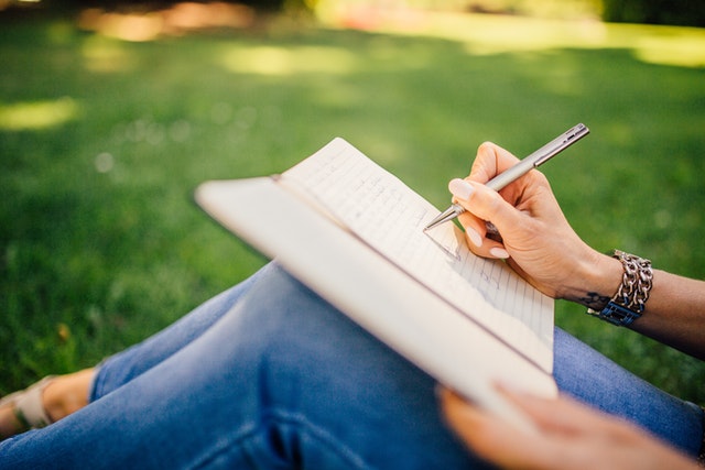image of woman sitting on grass writing in a journal